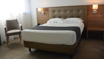 Ett hotellrum med en stor säng, en stol och två sängbord med lampor.