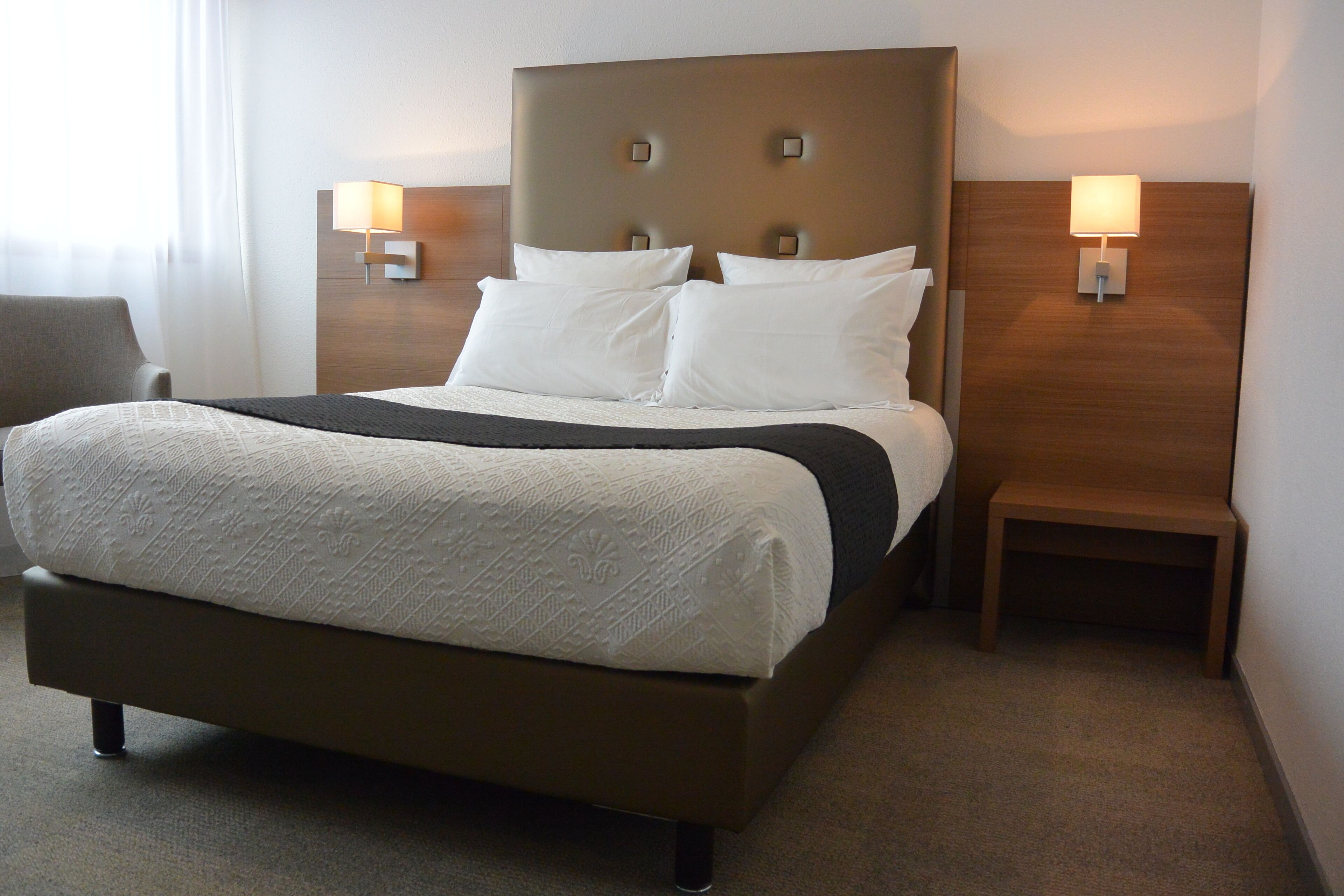 Habitación de hotel con una cama grande, dos mesitas de noche con lámparas, una silla y piso alfombrado.