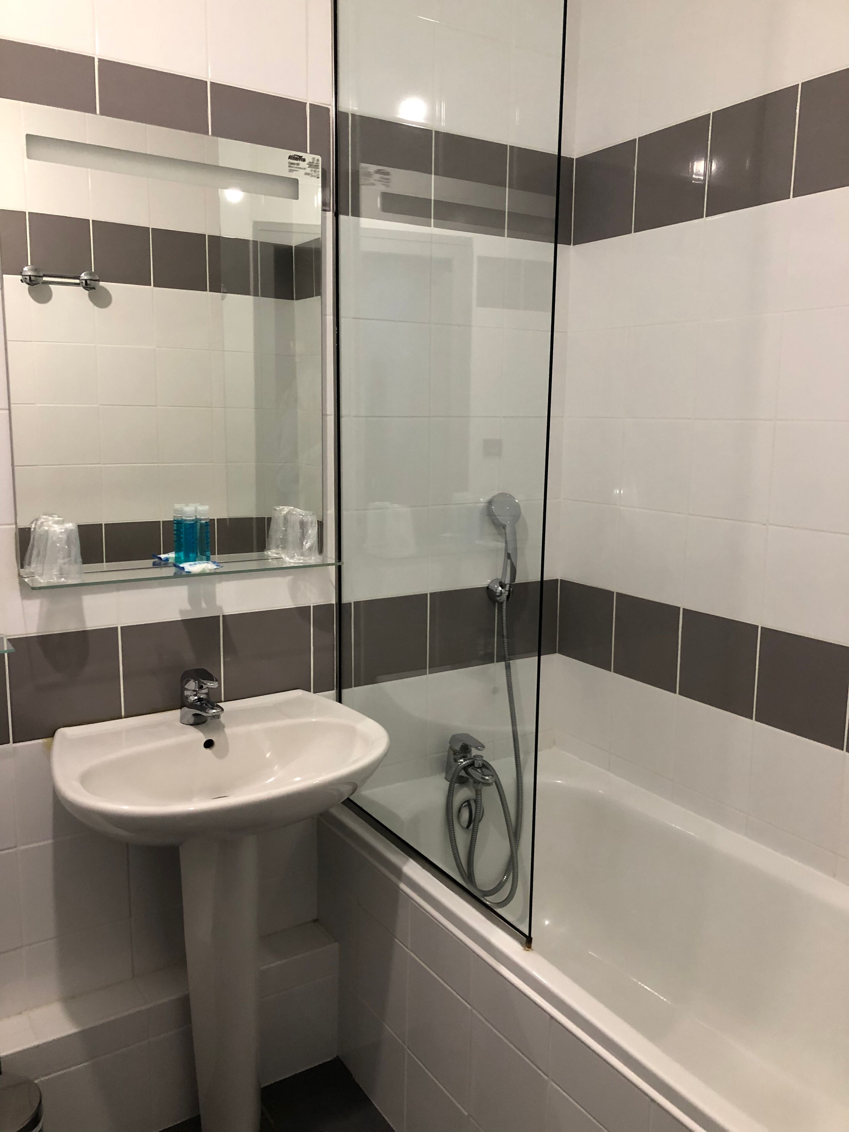 Ett badrum med en dusch som är avskärmad med glasväggar, ett handfat och en spegel ovanför handfatet.