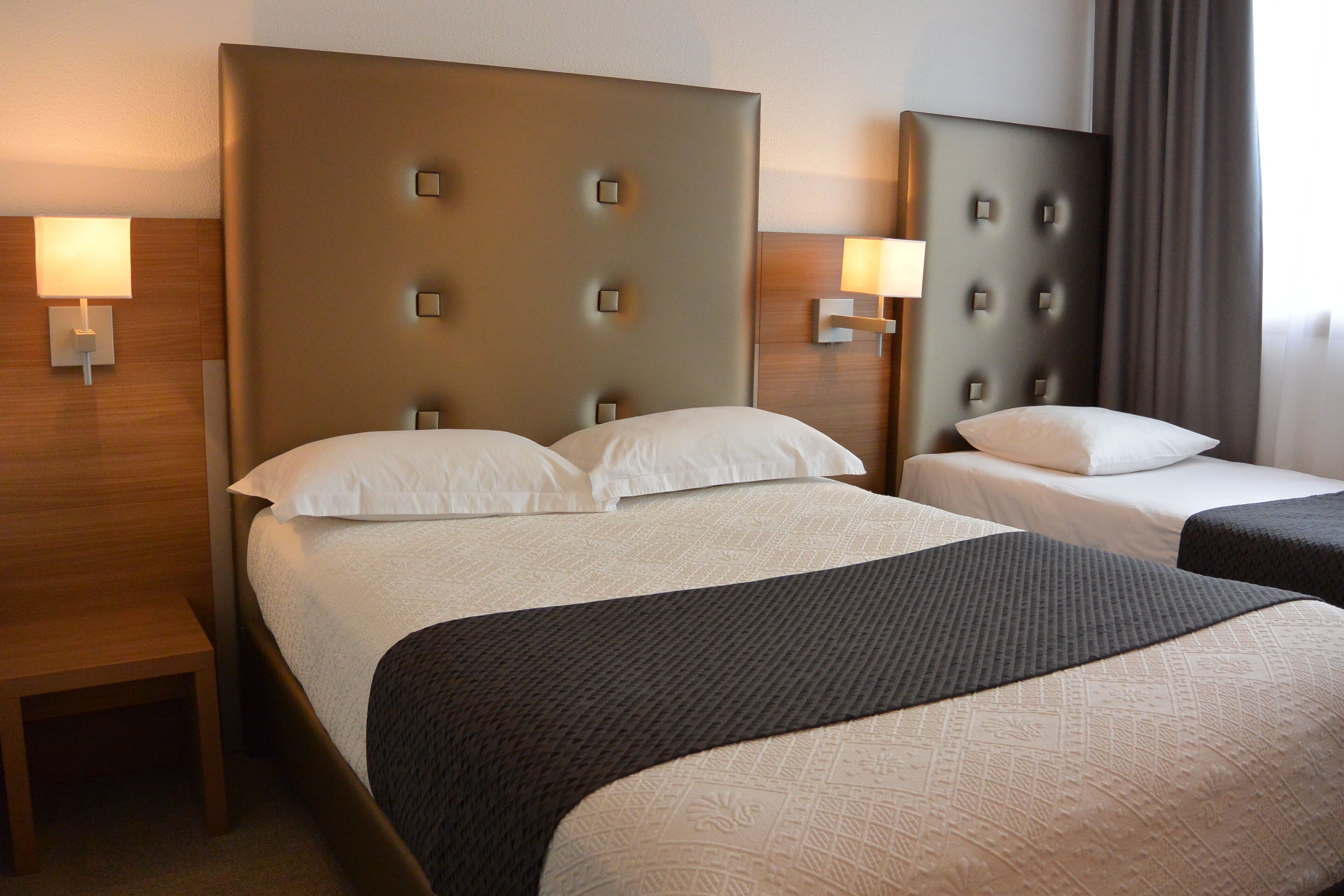 Una habitación de hotel con dos camas, cada una con cabecera y lámparas de noche.