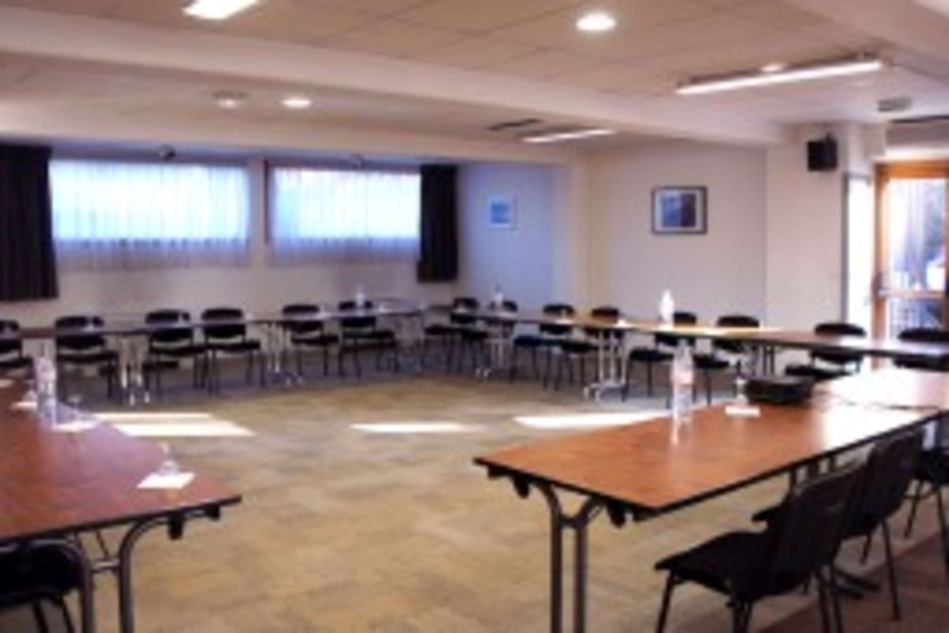 A conference room with a long table and chairs, large windows with curtains, and a framed picture on the wall.