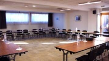 A conference room with a long table and chairs, large windows with curtains, and a framed picture on the wall.
