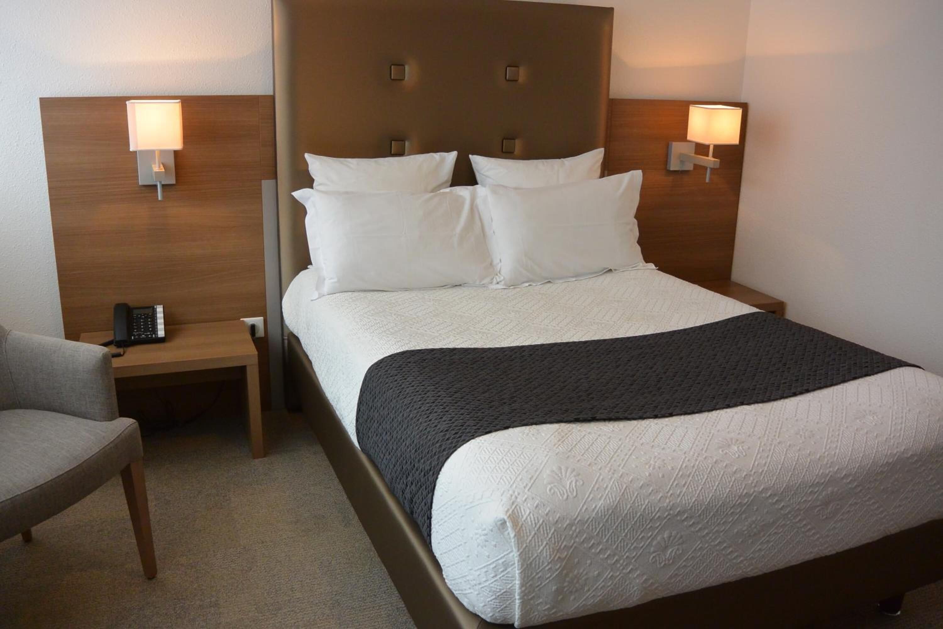 Une chambre d’hôtel comprenant un lit, deux lampes de chevet, une chaise et un bureau avec un téléphone.