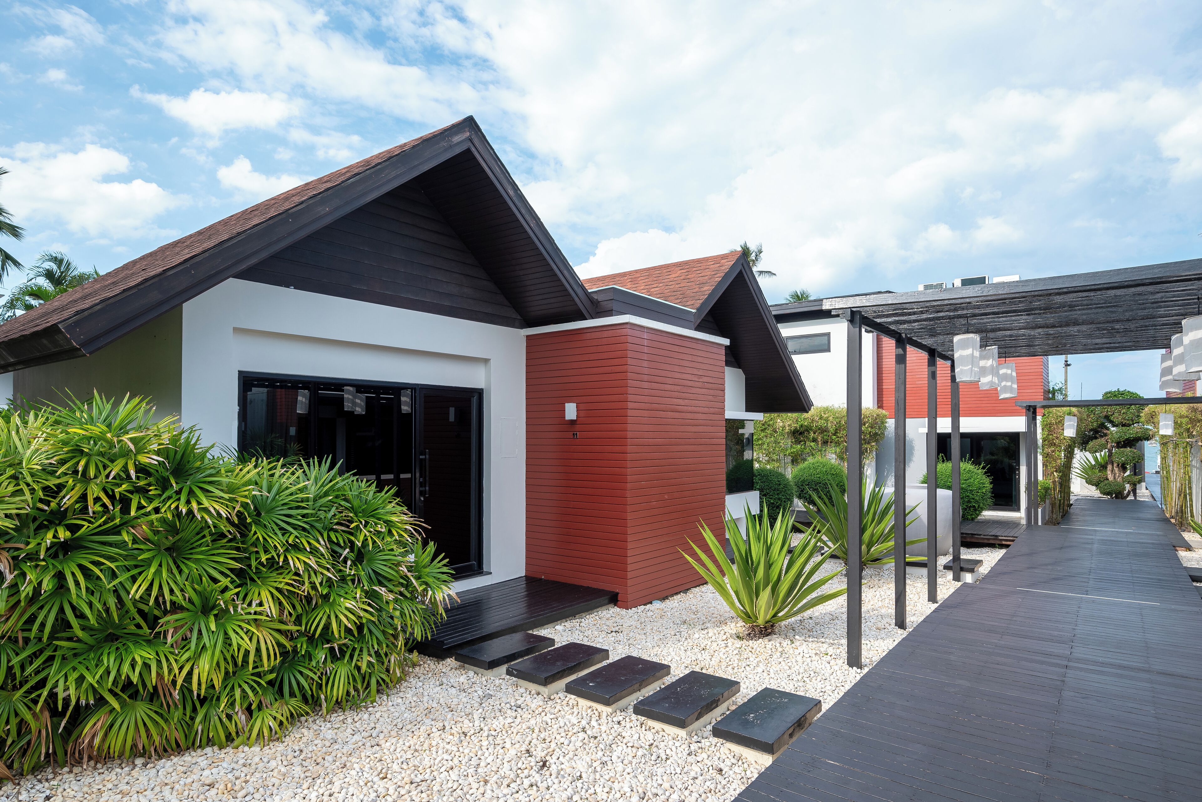 A modern house with a sloped roof, a red and white exterior, and a paved pathway leading to the entrance.