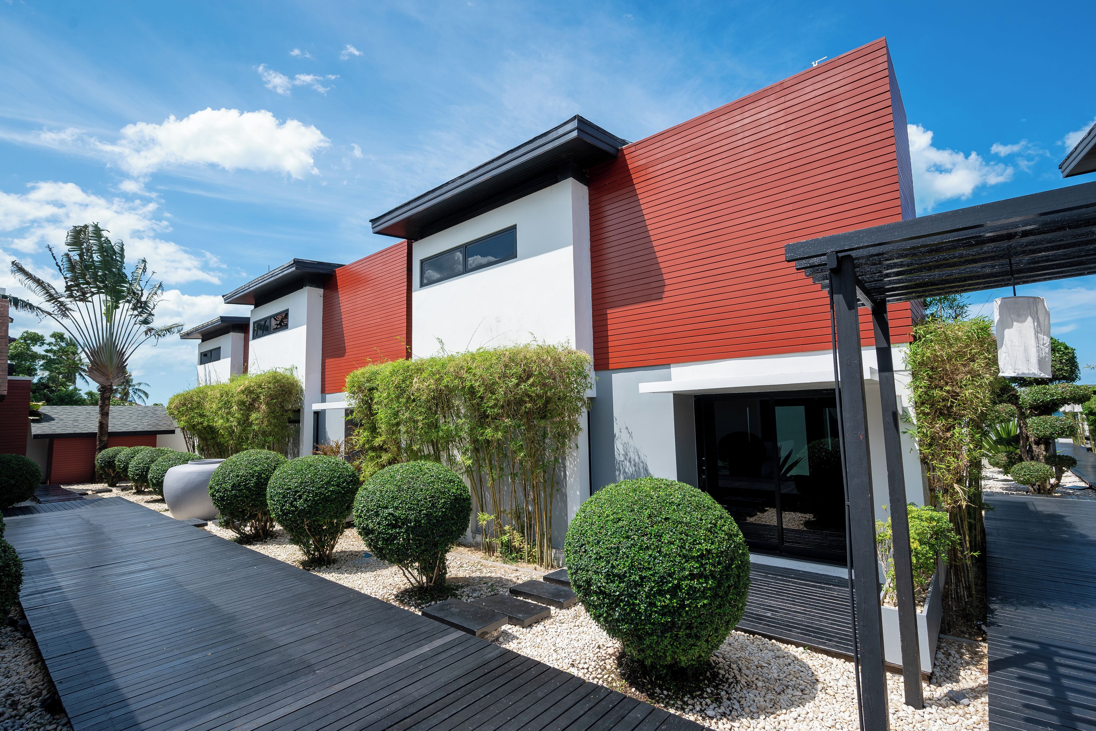 A modern building with a red and white facade, surrounded by well-maintained landscaping and a wooden deck.