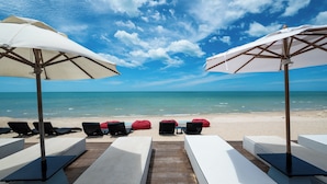 Ein Strandlounge mit weißen Liegestühlen und roten Sitzsäcken, weißen Sonnenschirmen und einer Holzterrasse, die zum Strand führt.