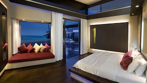 Ein modernes Schlafzimmer mit einem großen Bett, einer Sitzecke mit Kissen und Meerblick.
