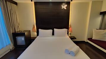 A hotel room with a large bed, two bedside tables, a nightstand with a lamp, a wall-mounted telephone, and a window with curtains.