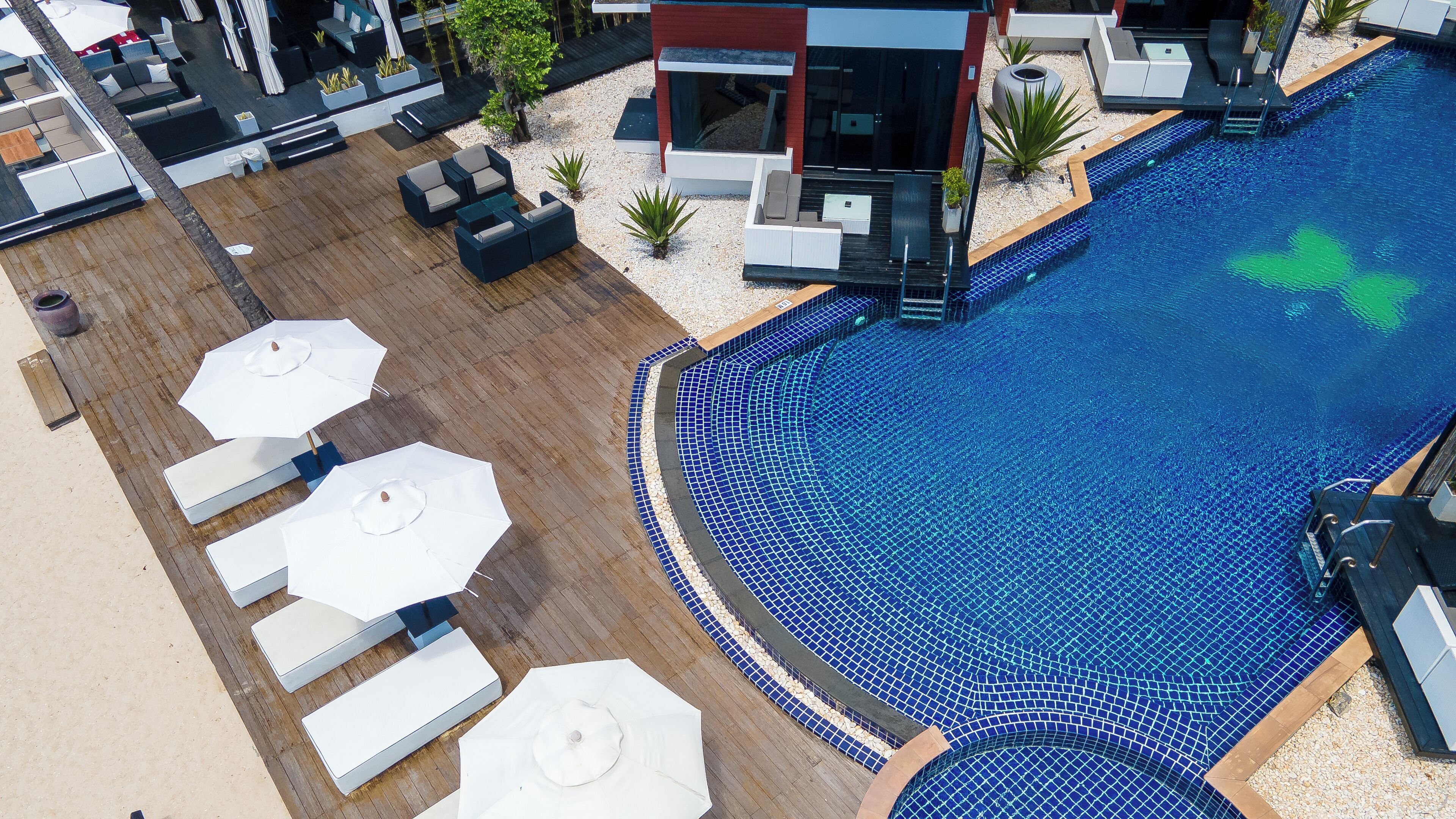 Un espace piscine aménagé sur le toit, avec des chaises longues et des parasols, entouré d’immeubles modernes.
