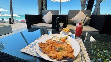 A dining table with a plate of fried fish, a drink, and condiments.