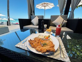 A dining table with a plate of fried fish, a drink, and condiments.