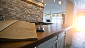 Un comptoir en bois avec une cloche, un carnet et un mur de pierres en arrière-plan.