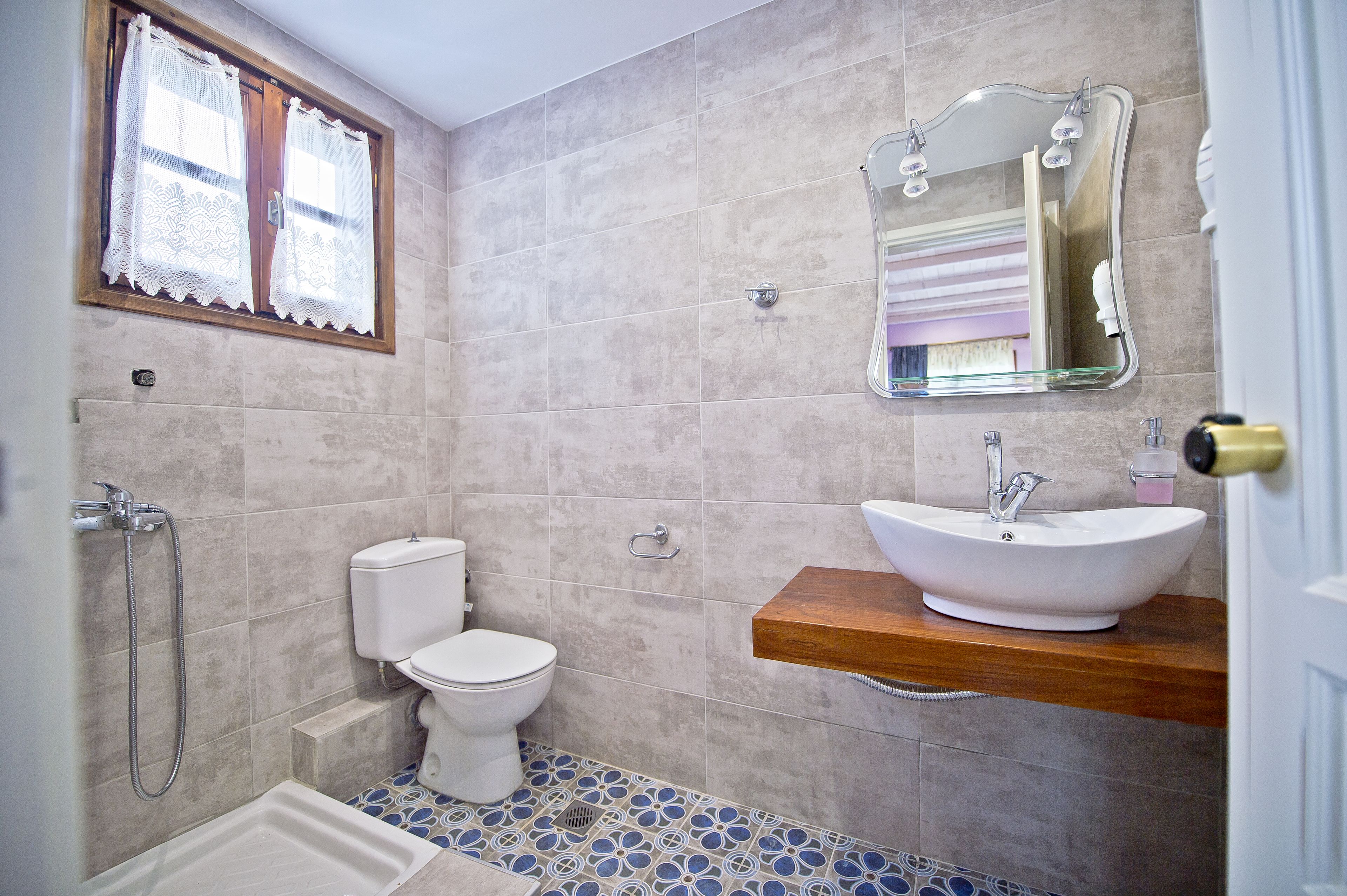 Ein Badezimmer mit Toilette, Waschbecken, Dusche und einem Fenster mit Spitzenvorhängen.