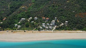 Vue aérienne d’une zone côtière avec des maisons construites sur une colline, surplombant une plage de sable et des eaux turquoise.
