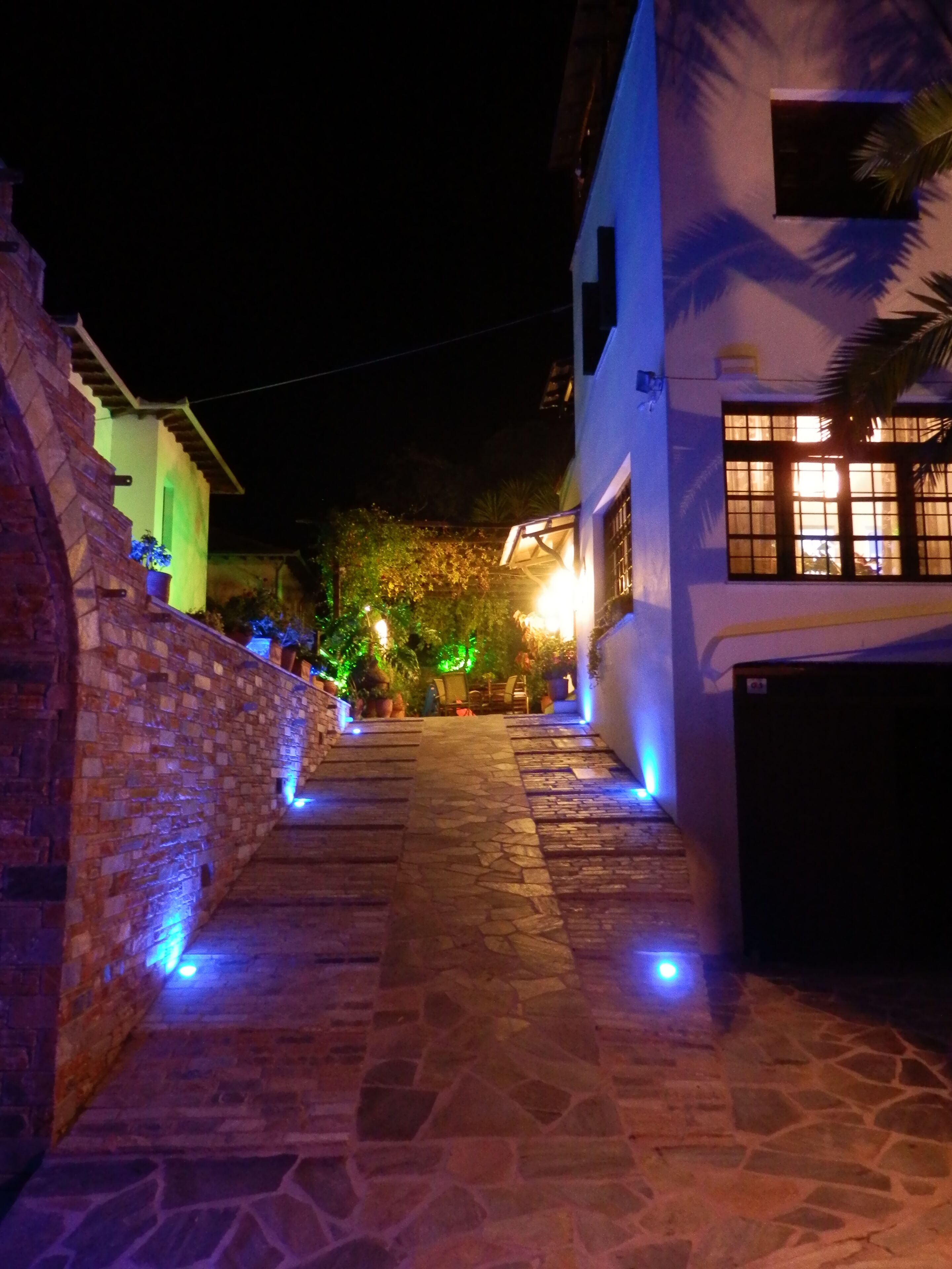 A narrow stone pathway leading to a building with a white facade and a window with a grid pattern.
