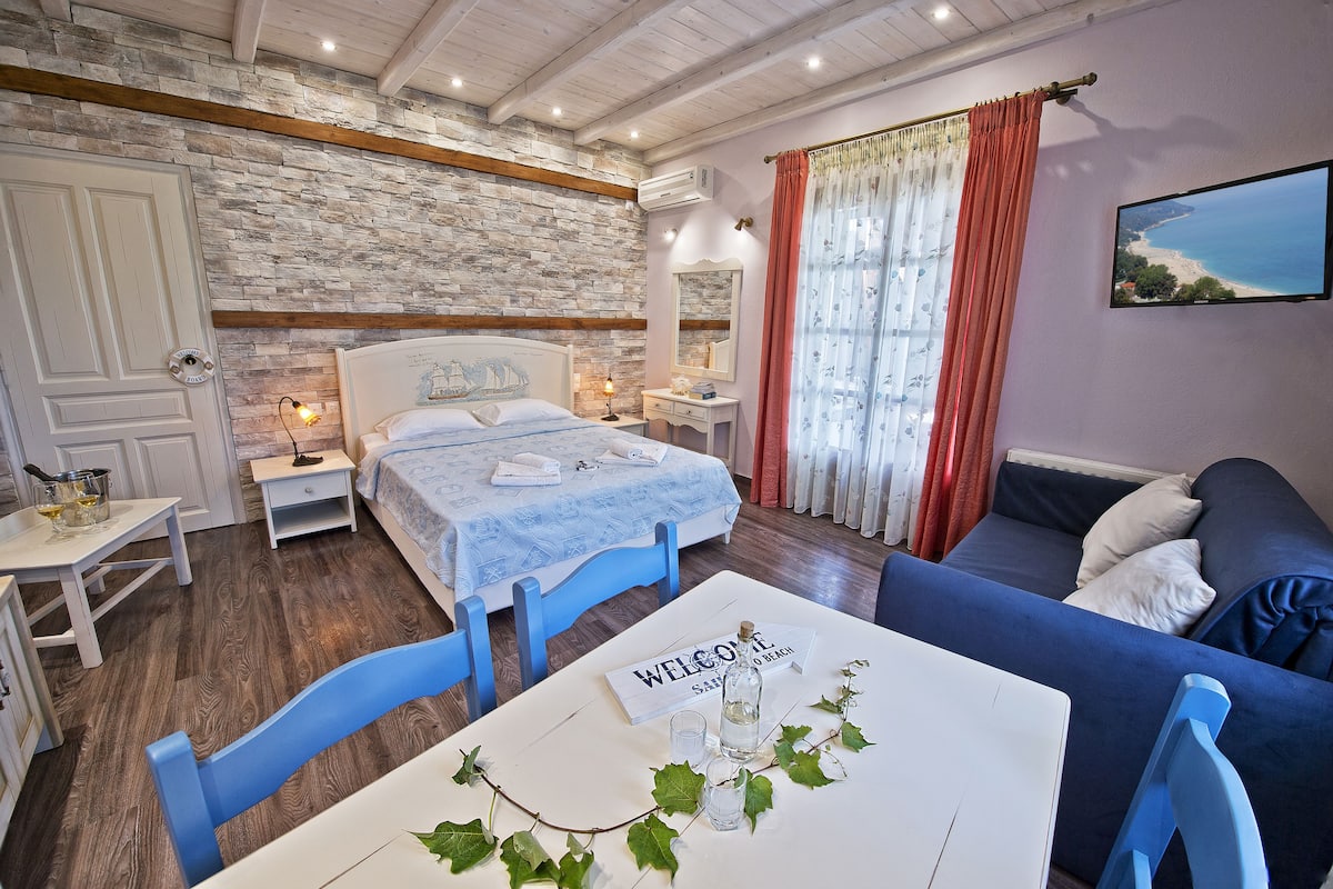 Un dormitorio con pared de piedra, una cama, un sofá, un televisor y una mesa con un cartel de bienvenida.