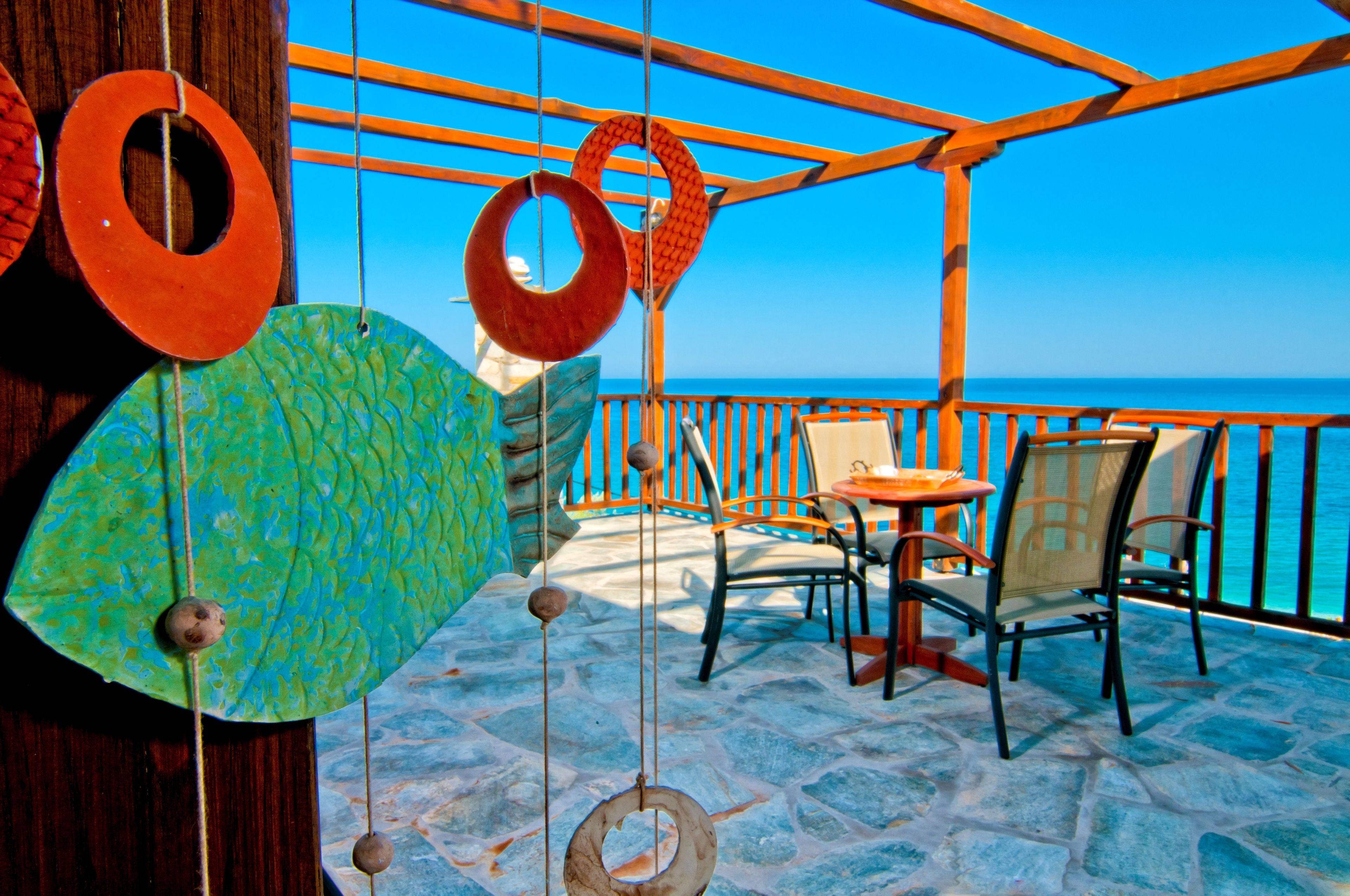 Een terras met stenen vloer, houten stoelen en tafels, met uitzicht op een heldere blauwe zee.