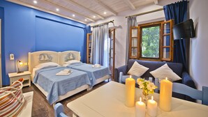 Une chambre d’hôtel avec deux lits, un canapé, une table avec des bougies et un téléviseur fixé au mur.