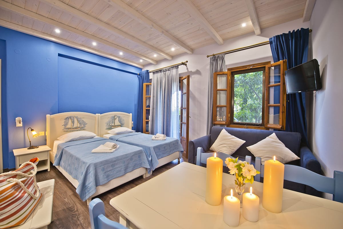 Habitación de hotel con dos camas, un sofá, una mesa con velas y un televisor montado en la pared.
