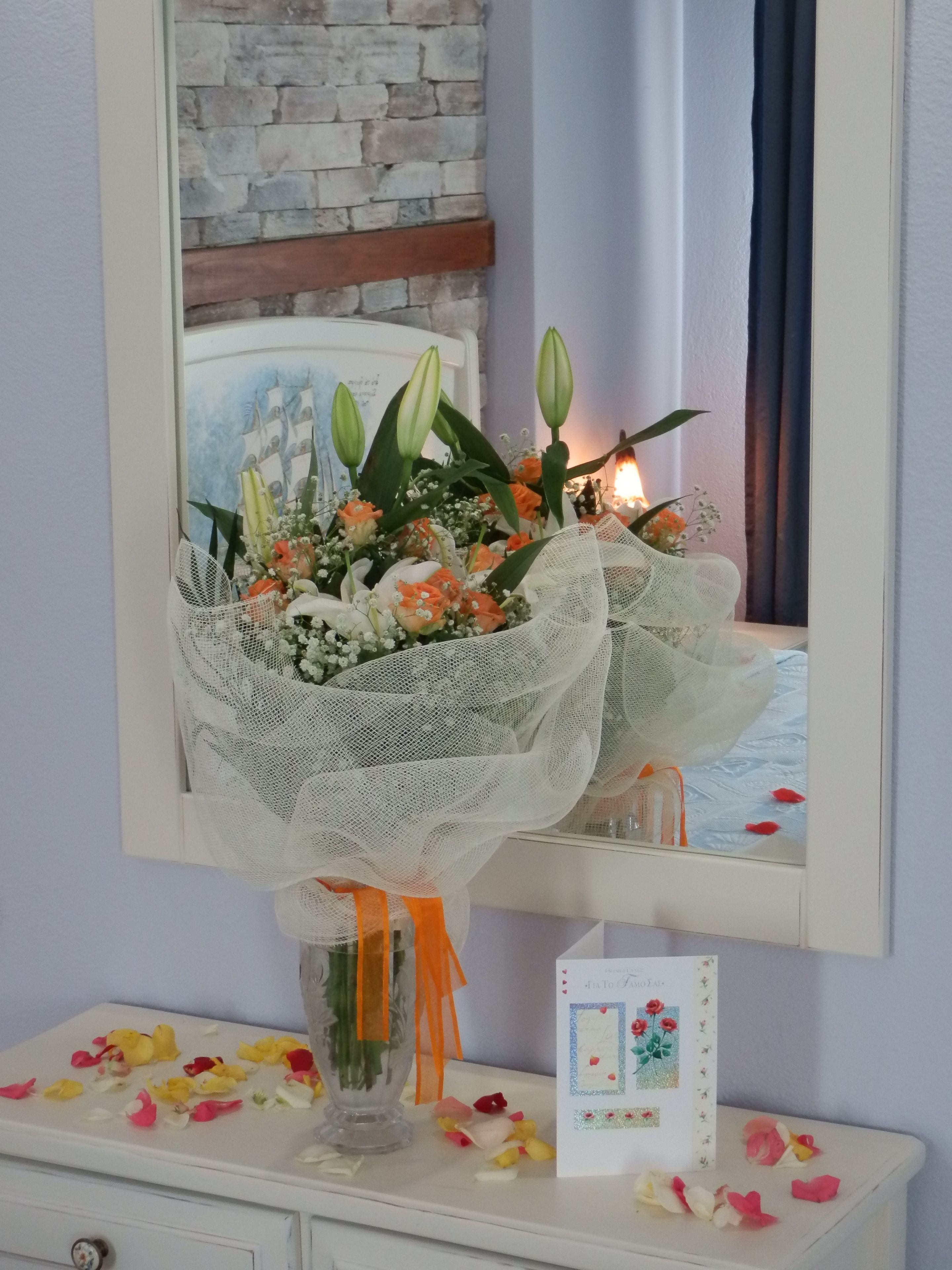 Een bloemenboeket in een vaas op een dressoir met een spiegel erboven.