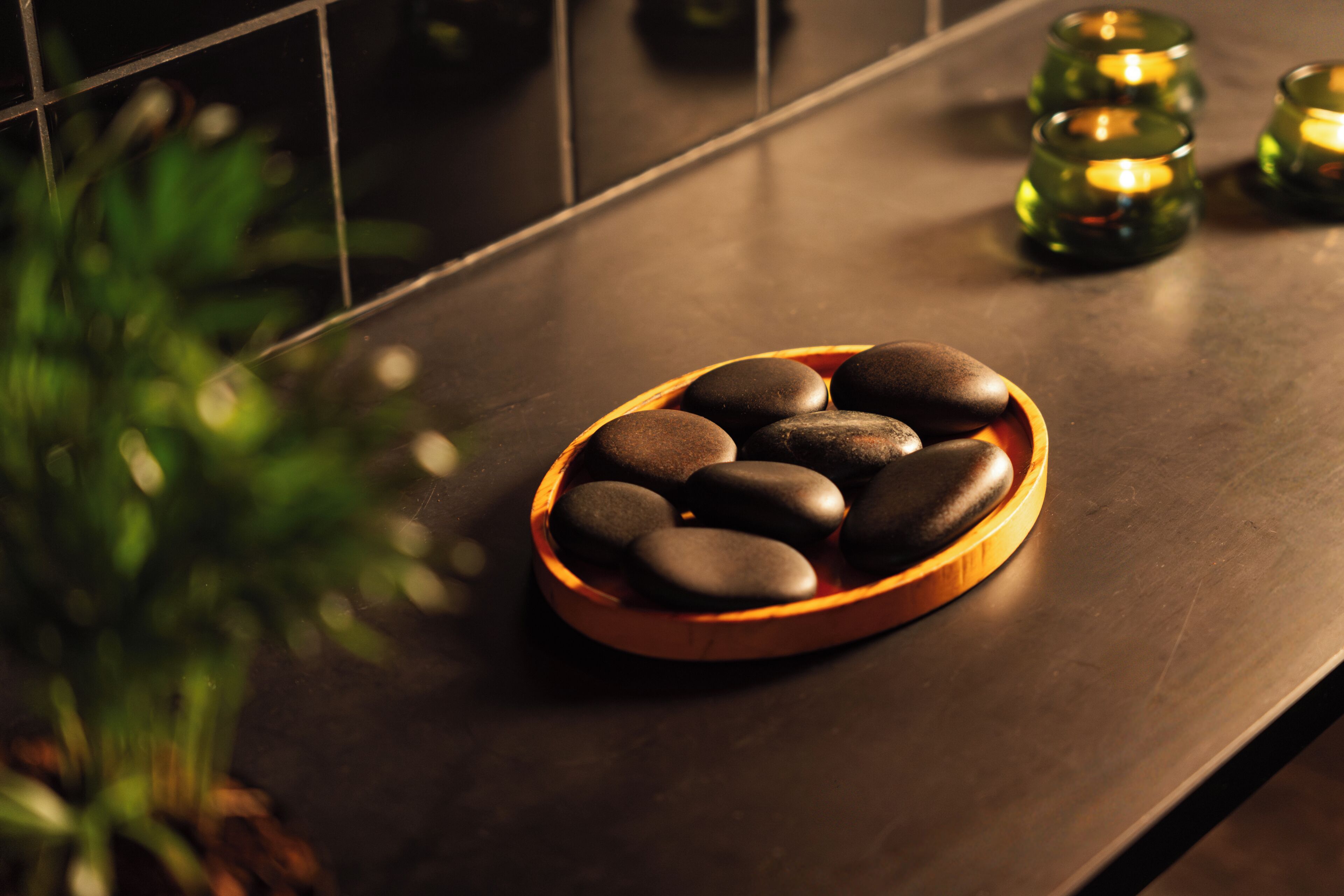 A bowl of smooth stones on a dark countertop with green glass candle holders in the background.
