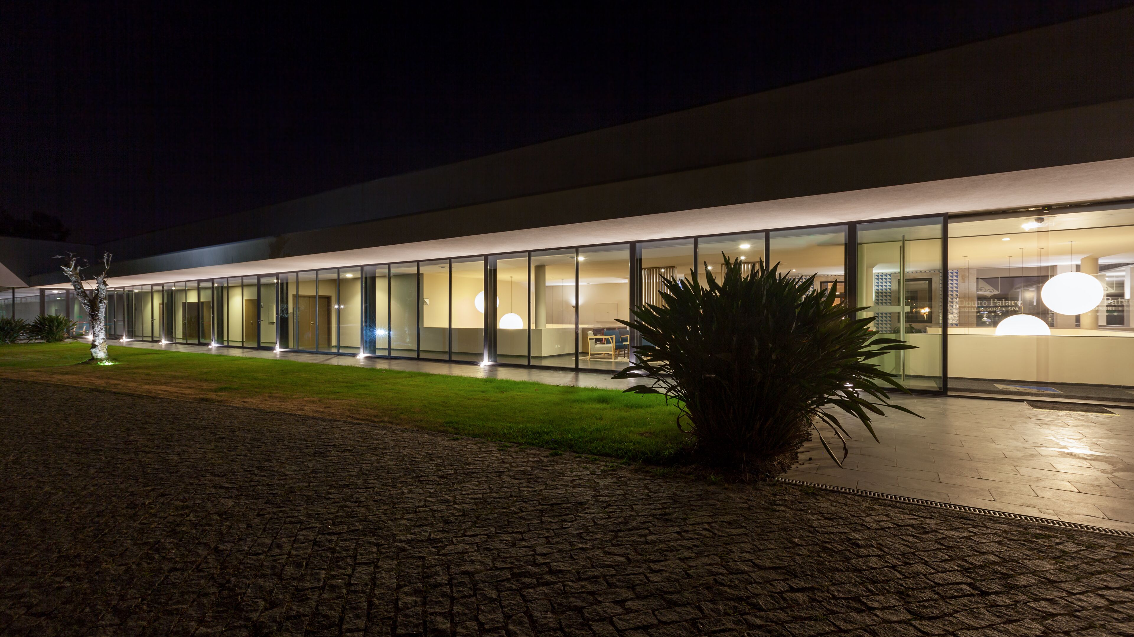 Um edifício moderno com fachada de vidro, uma área de recepção bem iluminada e entrada pavimentada.