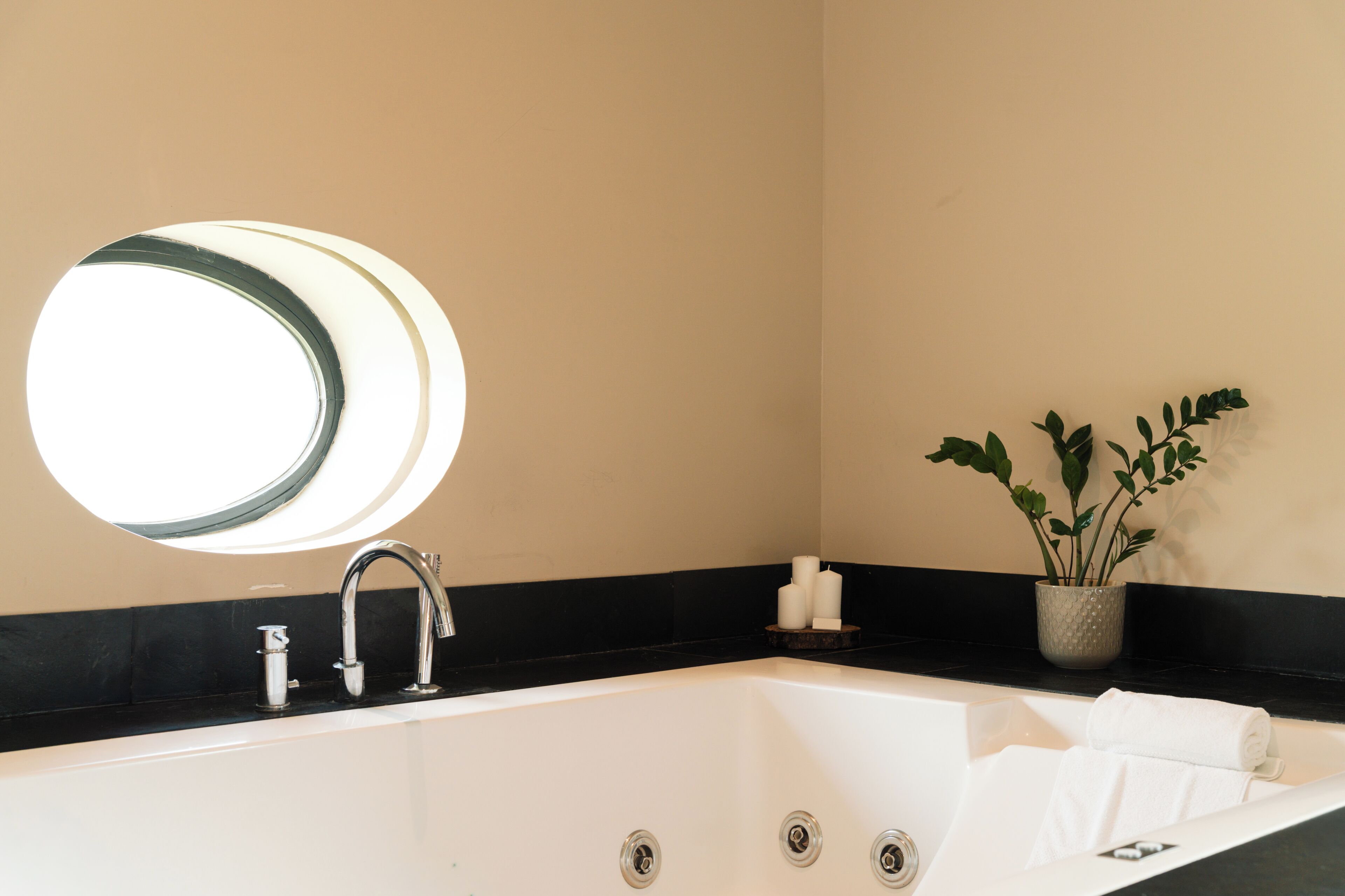 Un baño moderno con una bañera grande, un espejo redondo, un grifo, una planta en maceta y una pequeña estantería con velas.