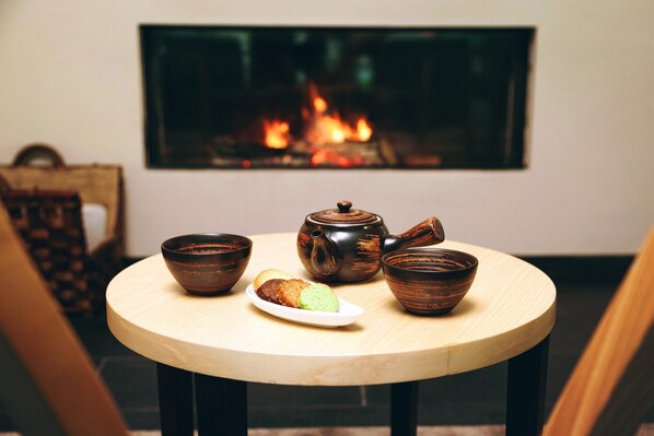 A round wooden table with a teapot, cups, and a plate with a pastry. A fireplace is visible in the background. - Douro Palace Hotel Resort and Spa (Baiao)