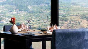 A dining table set with wine glasses, a vase with flowers, and a view of a hilly landscape. - Douro Palace Hotel Resort and Spa (Baiao)
