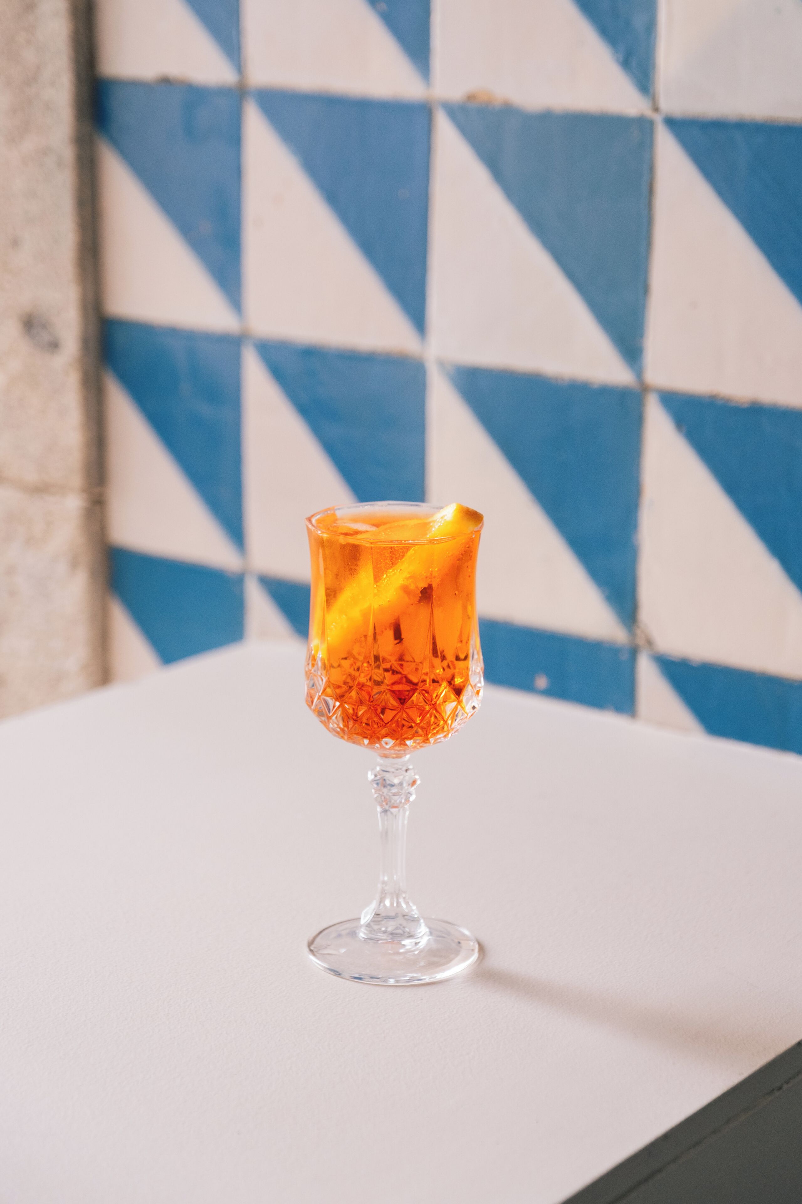 A glass with a drink on a table against a blue and white tiled wall.