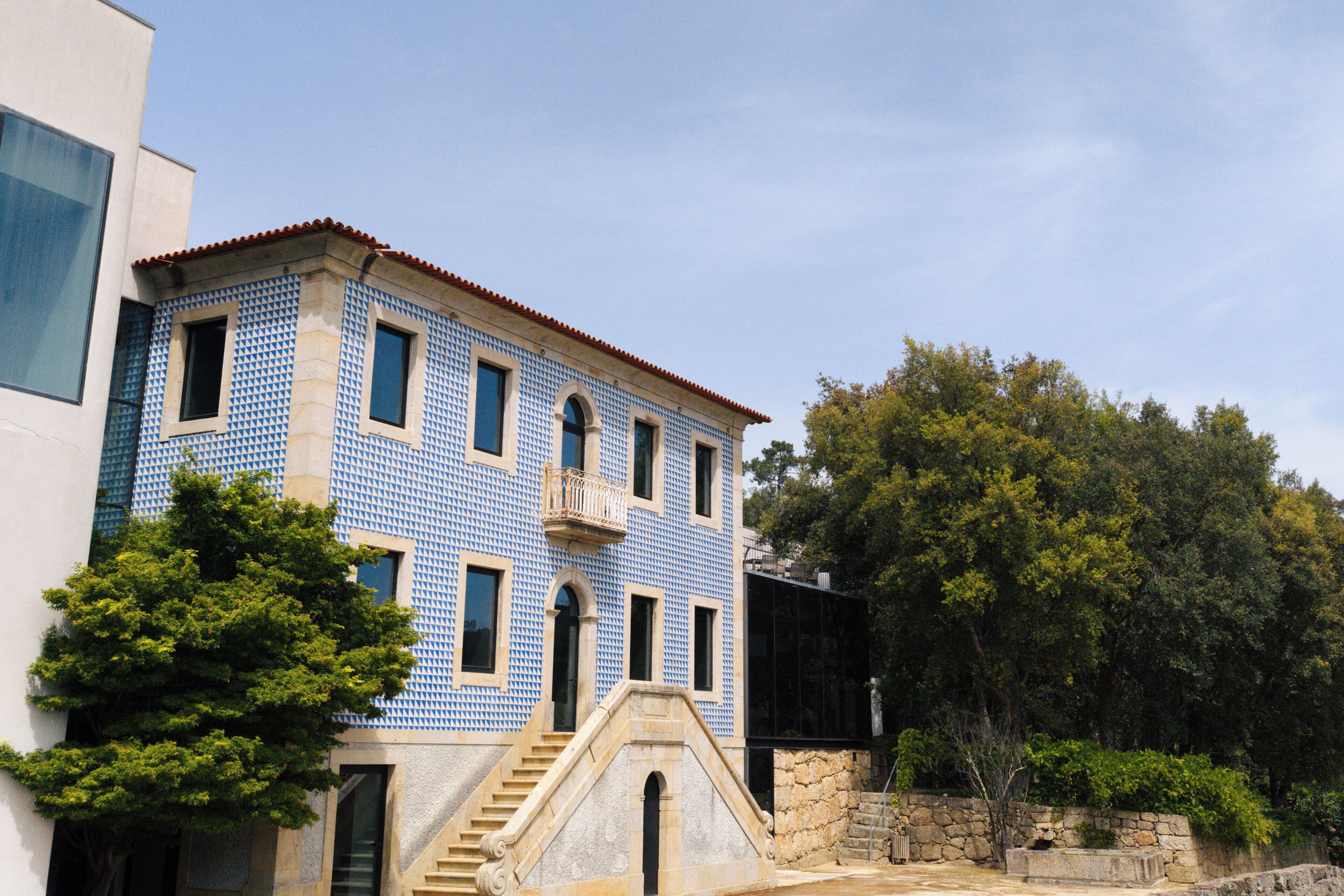 A building with a tiled facade, a staircase leading to the entrance, and a tree in the foreground.