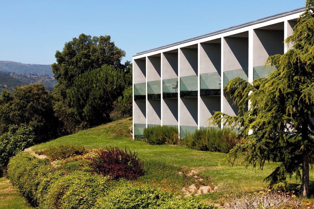 A modern building with a geometric facade, surrounded by lush greenery and trees.