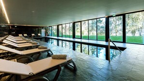 A modern indoor pool area with sun loungers and large windows overlooking a green landscape. - Douro Palace Hotel Resort and Spa (Baiao)