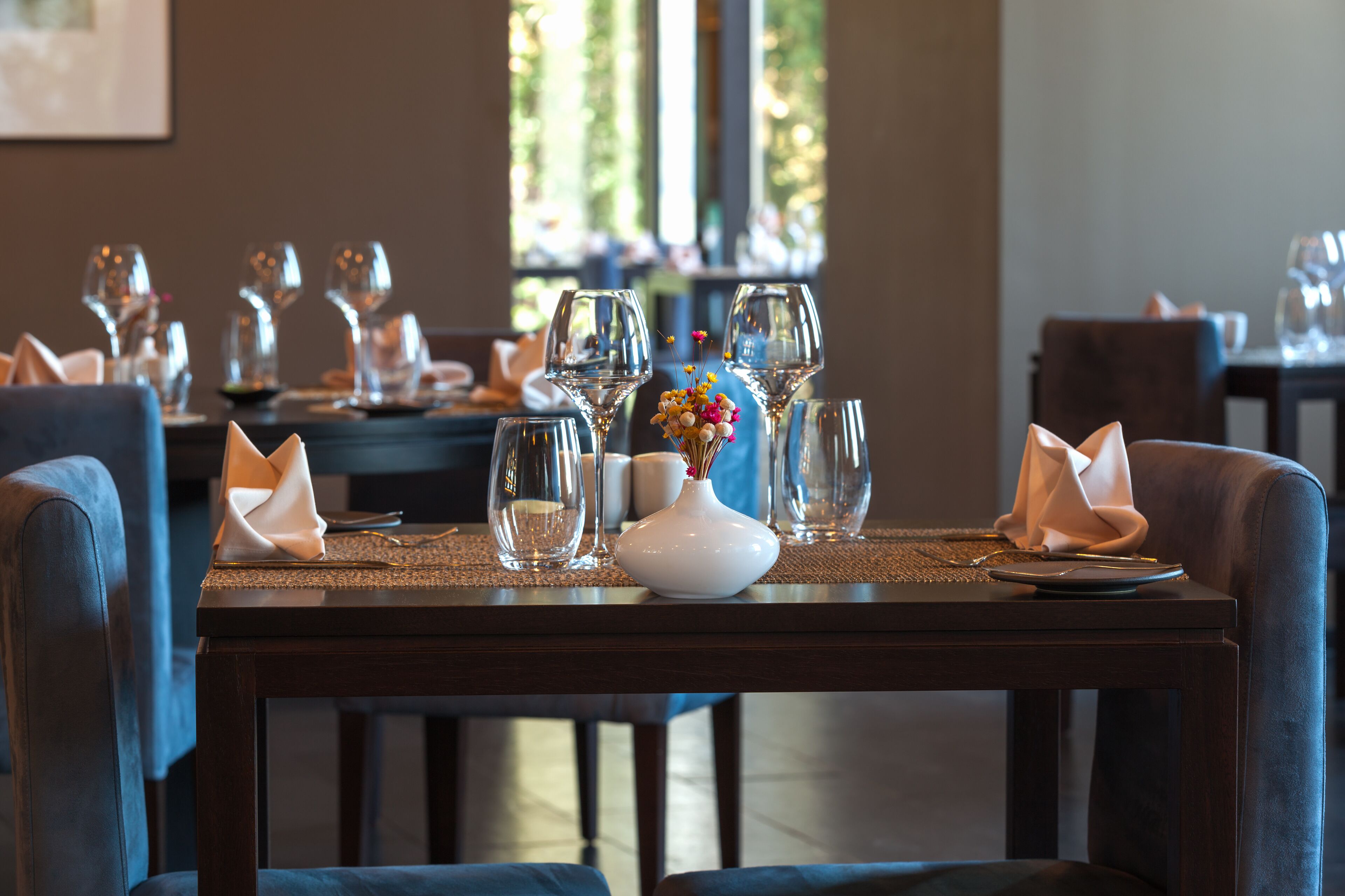 A dining table set with wine glasses, a vase with flowers, and folded napkins.