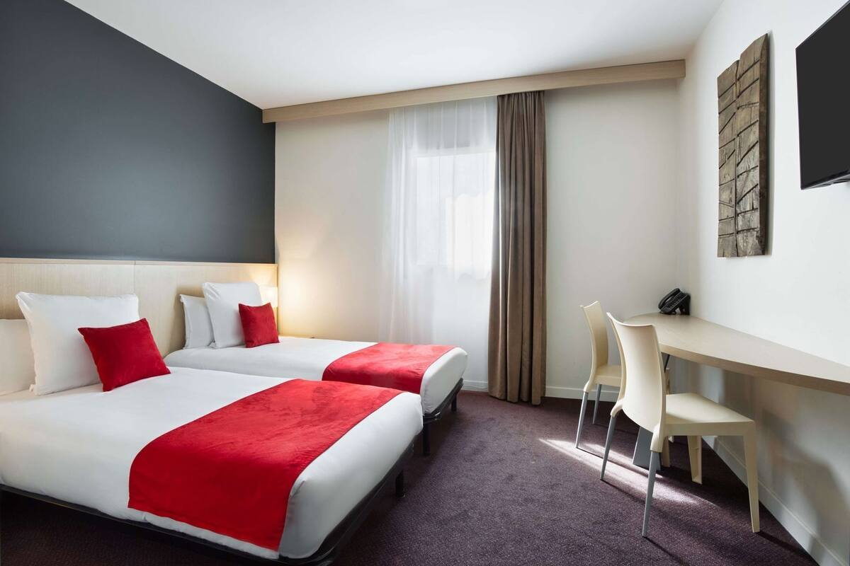 A hotel room with two beds, a desk, a chair, a phone, and a TV.