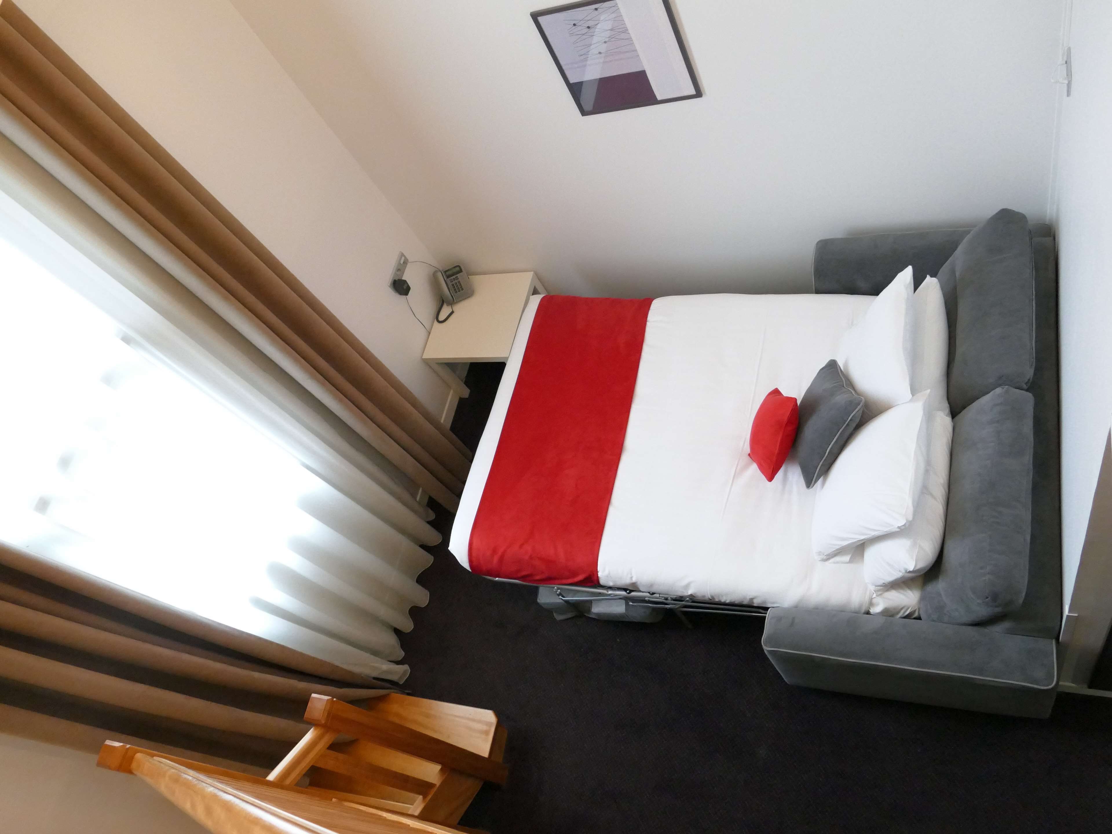A hotel room with a bed, a desk, a chair, and a window with curtains.