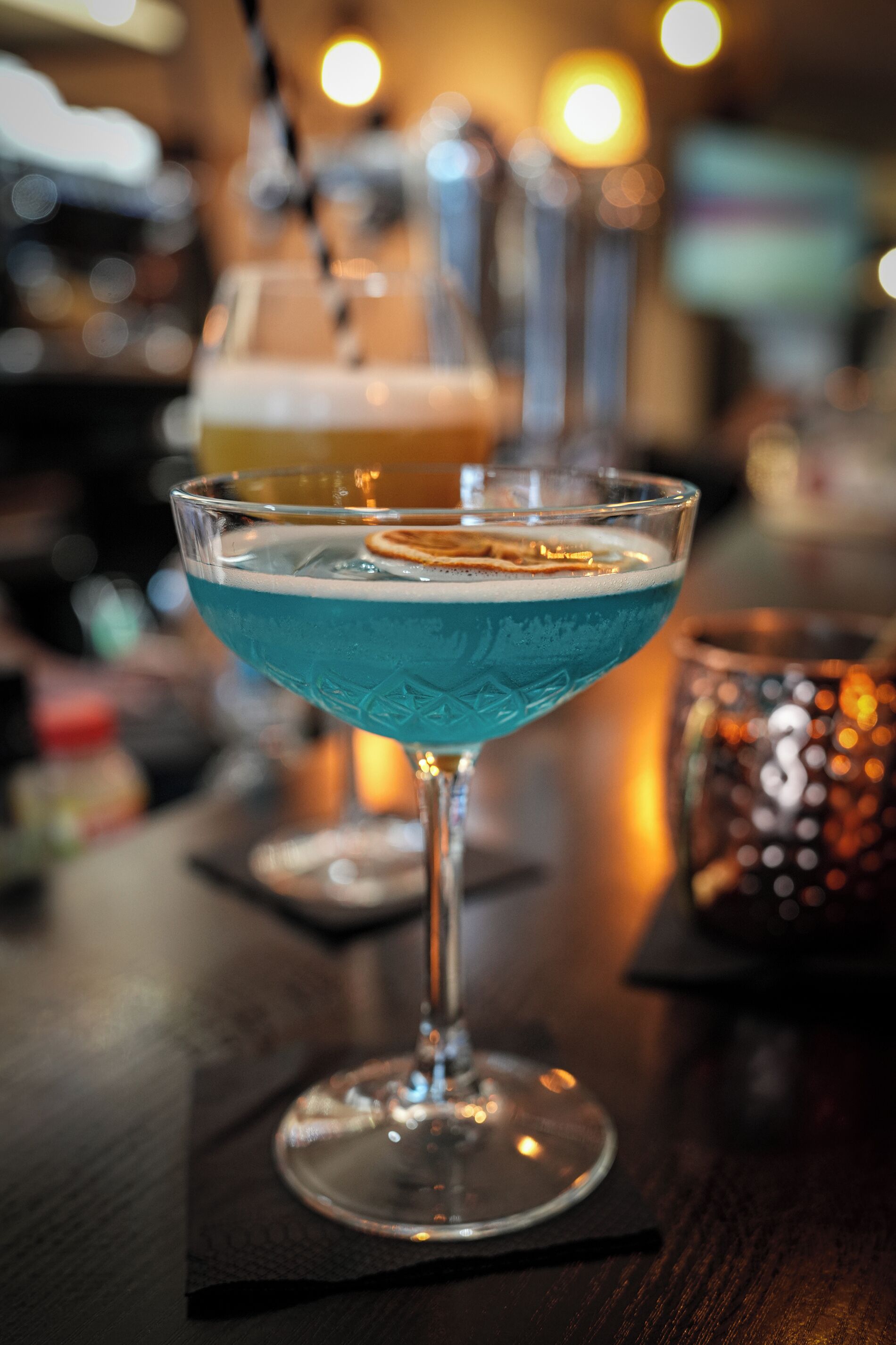 A cocktail glass with a blue liquid on a bar counter.