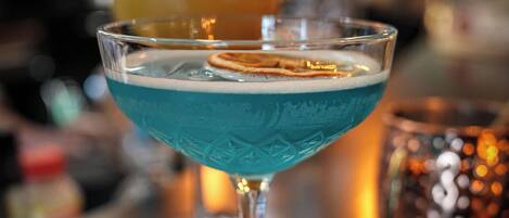 A cocktail glass with a blue liquid on a bar counter.