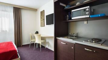 A hotel room with a bed, a desk, a chair, a kitchenette with a microwave, and a sink.