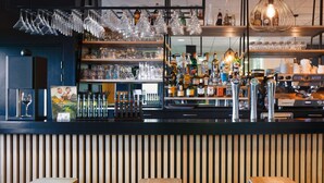 A bar area with wooden slats, stools, and shelves stocked with bottles and glasses. - Sure Hotel by Best Western Nantes Beaujoire (Nantes)