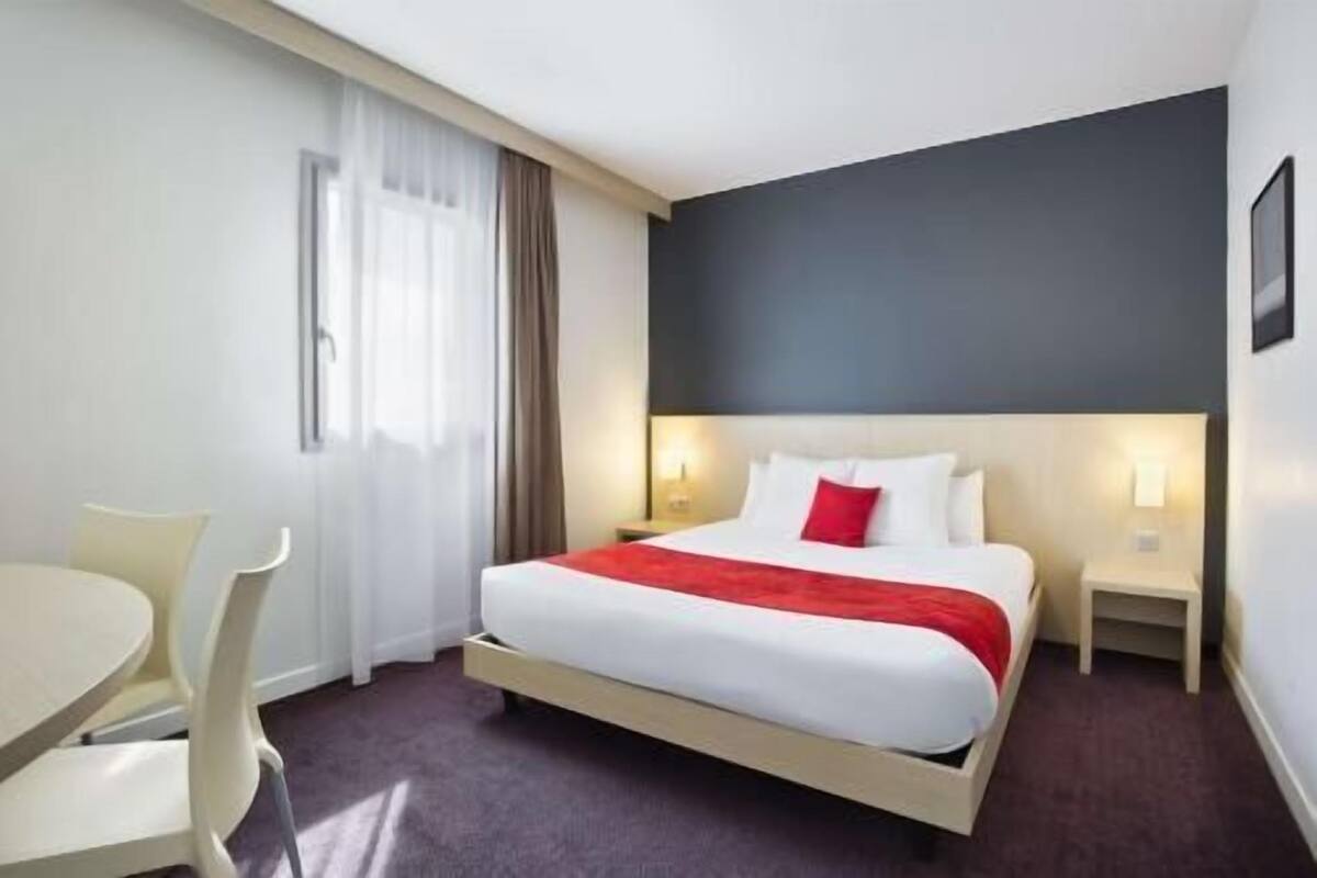 A hotel room with a bed, a desk, a chair, and a window with curtains.