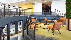 A modern indoor seating area with a curved railing, orange chairs, and a staircase leading to an upper level. - Sure Hotel by Best Western Nantes Beaujoire (Nantes)