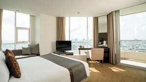 Une chambre d’hôtel moderne dotée d’un grand lit, d’un bureau avec une télévision et offrant une vue sur la ville grâce à de grandes fenêtres.
