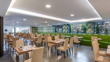 Un comedor moderno con varias mesas y sillas, asientos verdes y un mural decorativo.