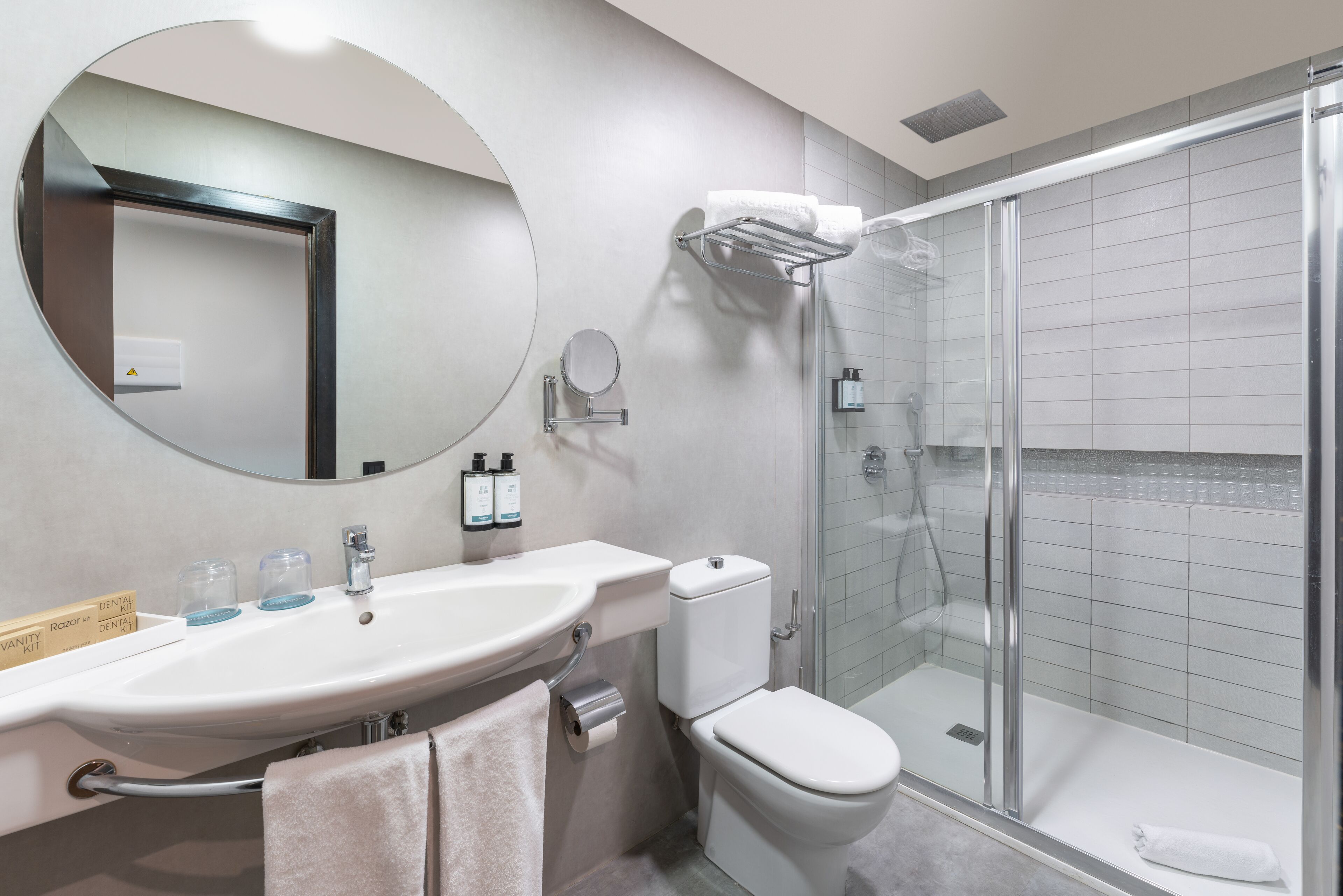 Ein modernes Badezimmer mit rundem Spiegel, Waschbecken, Toilette und einer Duschkabine.
