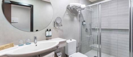 Un baño moderno con un espejo redondo, un lavabo, un inodoro y una ducha con mampara de vidrio.