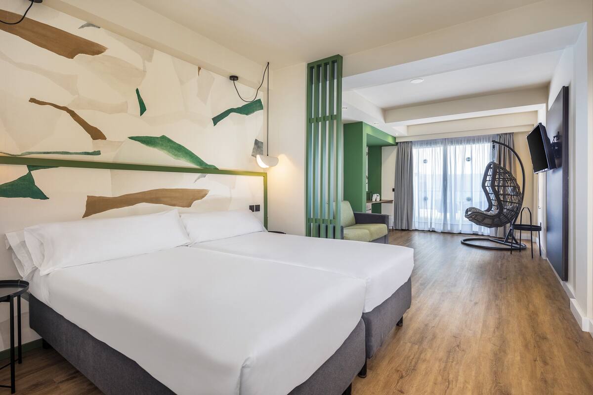 A hotel room with a large bed, a desk, a chair, and a TV.