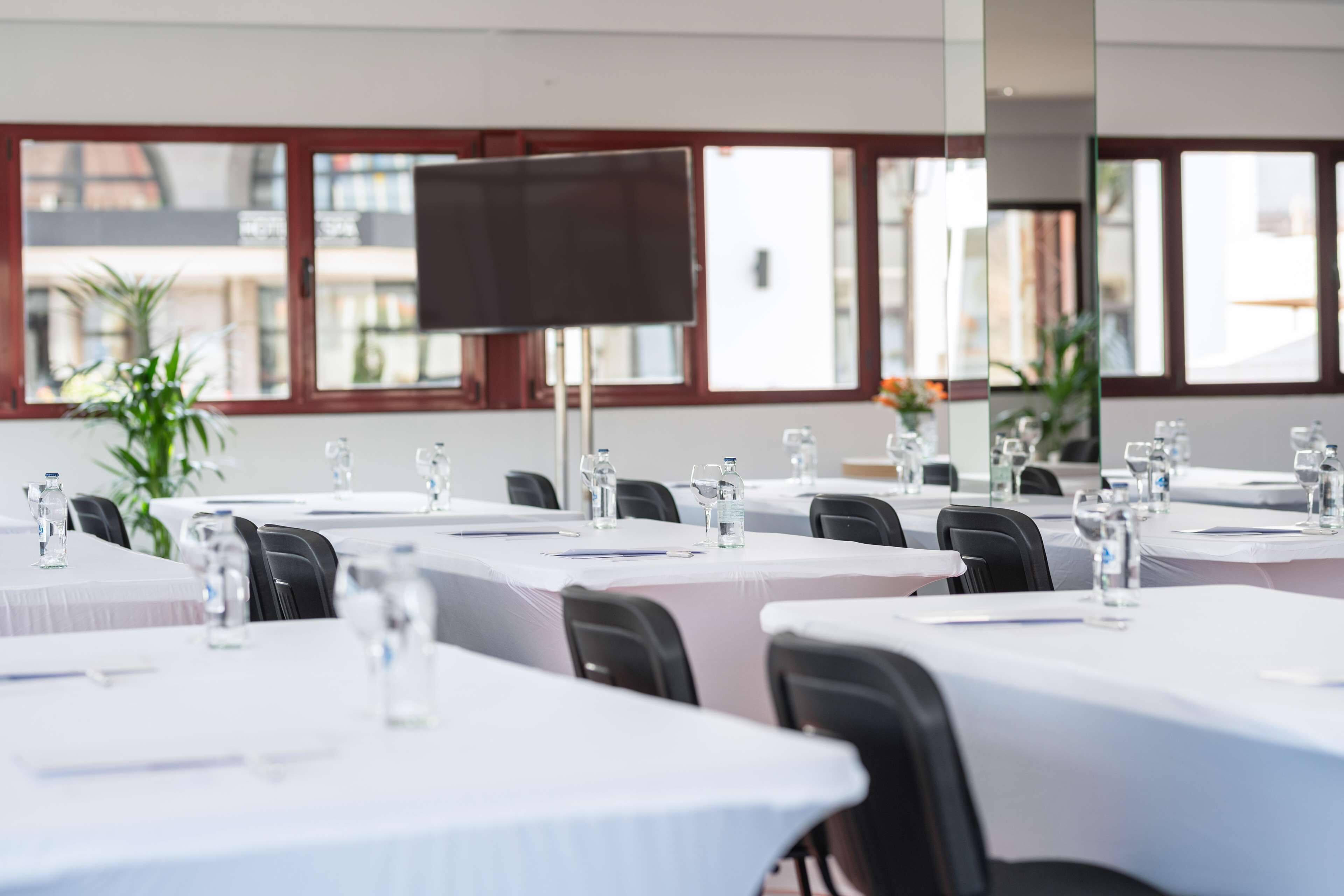 A conference room with tables set for meetings, equipped with water bottles and pens, and large windows offering a view of the outside.