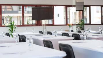 A conference room with tables set for meetings, equipped with water bottles and pens, and large windows offering a view of the outside.
