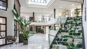 A spacious lobby with a high ceiling, a staircase with a tropical leaf pattern, and a seating area with a modern chair. - Occidental Roca Negra – Adults Only (Agaete)